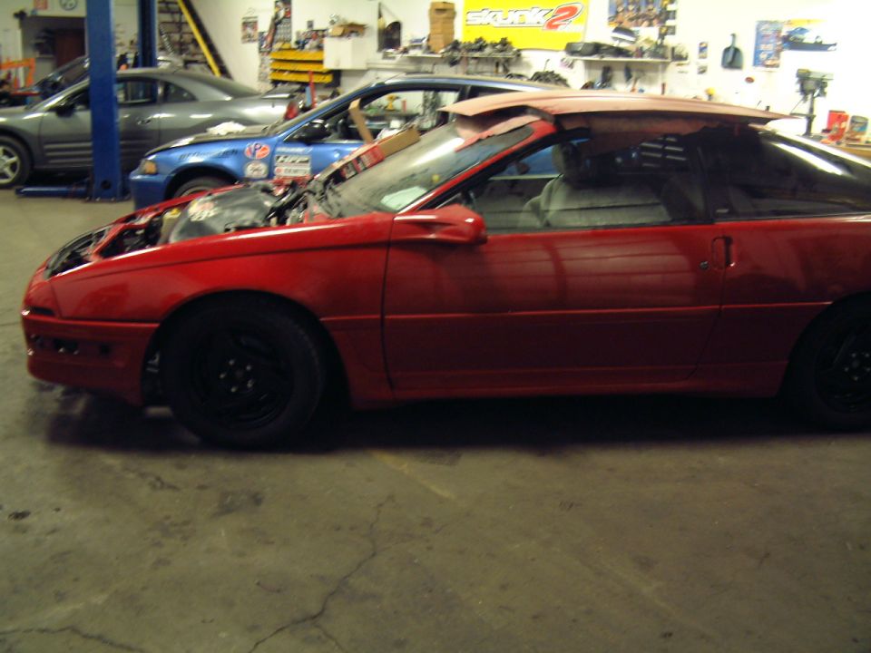 red sports car with hood open, another blue car and gray car behind it in a garage