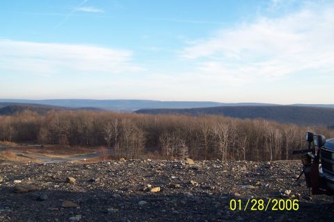 1979 Ford Bronco - A truck is parked on a rocky overlook, with a view of rolling hills and a wooded valley under a clear blue sky.