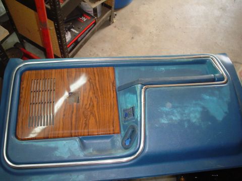 1984 Ford Bronco - Close-up of a blue car door panel a wood-grain accent and chrome trim, likely for a classic vehicle.