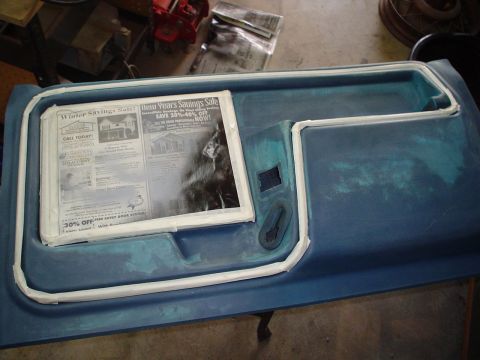 1984 Ford Bronco - A blue door panel is shown with a newspaper placed inside its recess, and a black handle visible.