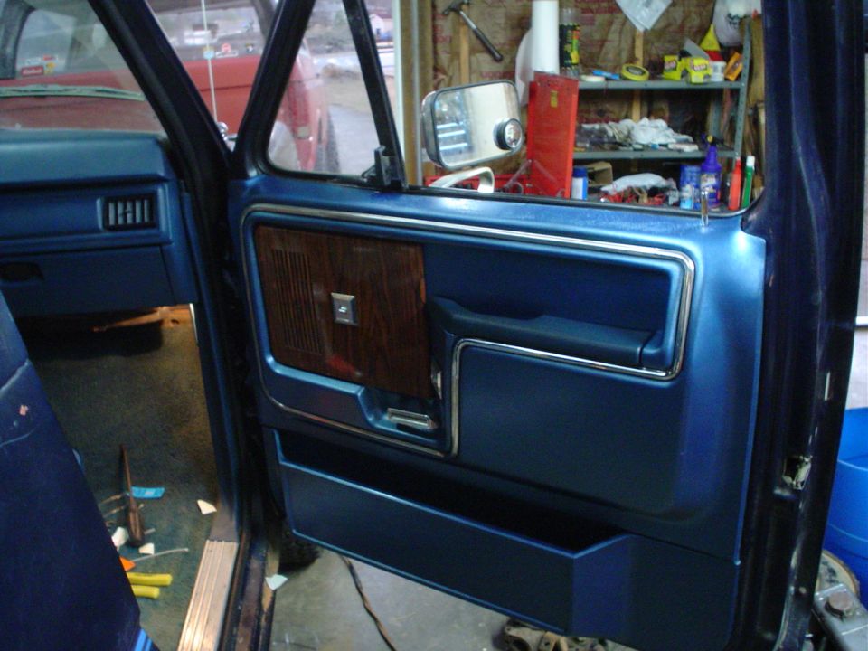 Open blue truck door interior panel with woodgrain trim in a garage