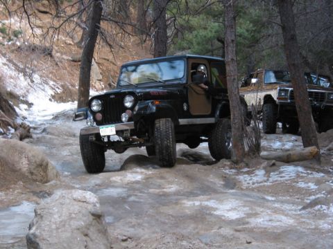 1981 Ford Bronco - A Jeep navigates a challenging off-road path, with another vehicle following closely behind.