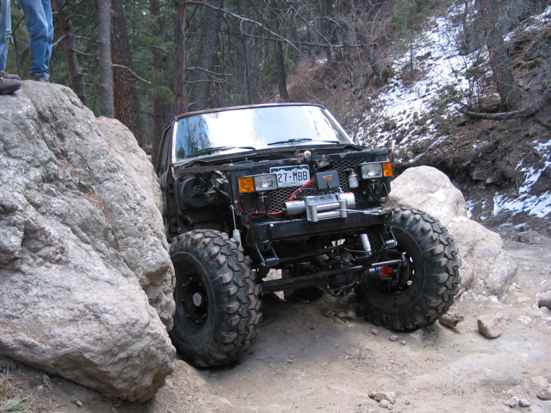 Hoodless dark 4x4 with front winch flexing off a boulder on a snowy forest trail