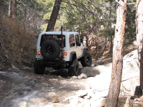 1981 Ford Bronco - White Jeep Wrangler navigates a challenging rocky trail, with a 'FOR SALE' sign visible in the rear window.