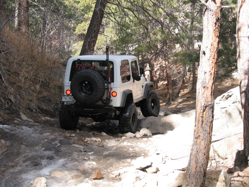 White Jeep Wrangler with 'FOR SALE' sign on rocky trail