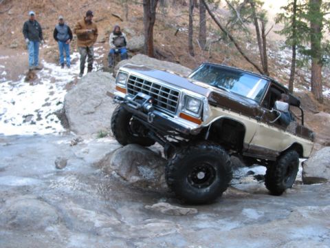1981 Ford Bronco - A modified Ford Bronco navigates a rocky, icy terrain with onlookers watching.