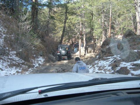 1993 Ford Bronco - Two vehicles navigate a challenging off-road path through a wooded area with scattered snow.