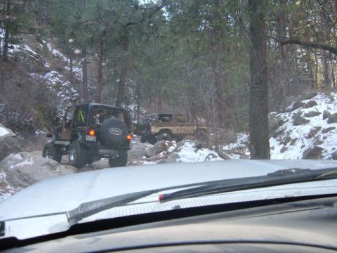 1993 Ford Bronco - Two off-road vehicles navigate a rocky, snow-dusted path through a forest.