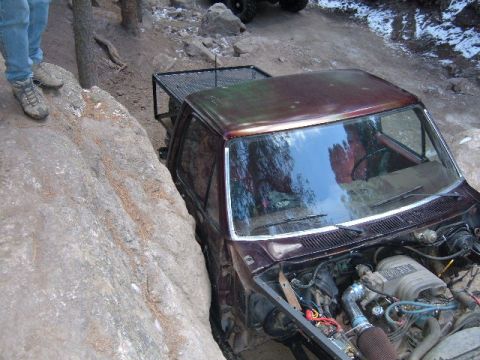 1993 Ford Bronco - A brown Ford Bronco is navigating a rocky trail, with its hood open and front tires wedged between large rocks.