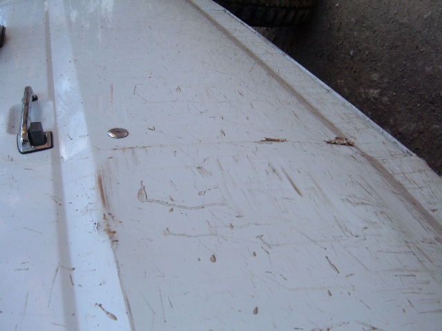 Scratched and scuffed white body panel with chrome latch and rust-colored streaks