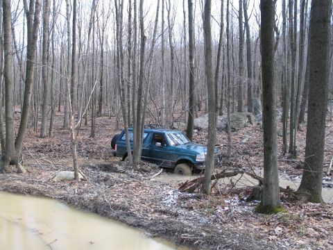 1995 Ford Bronco - A 1995 Ford Bronco navigates a challenging muddy path through a dense forest.