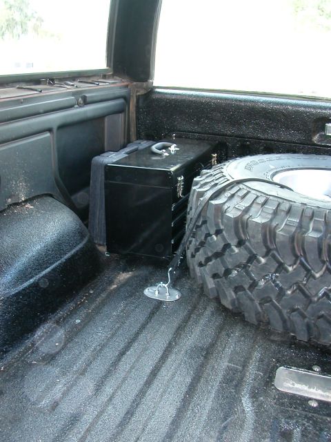 1984 Ford Bronco - Spare tire and toolbox stored in the rear cargo area of a vehicle.
