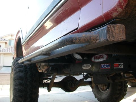 1984 Ford Bronco - This photo shows the underside of a modified off-road vehicle, prominent rock sliders and large tires.