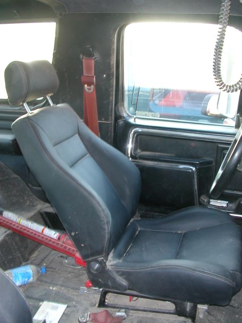 1984 Ford Bronco - The interior of the vehicle shows a black leather seat with red stitching and a red seatbelt.