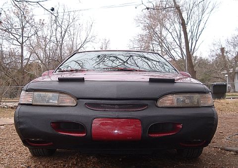 1994 Ford Thunderbird - The front of a red 1994 Ford Thunderbird is shown, partially covered by a black car bra.