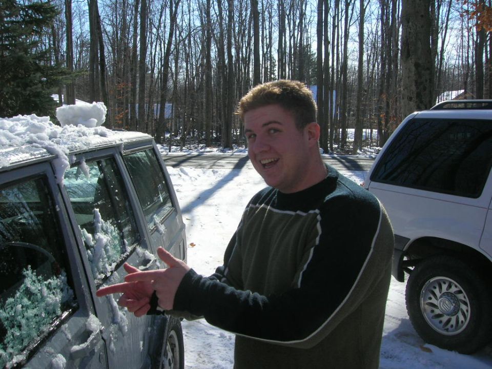 Guy in front of a snow-covered SUV, another white SUV behind him