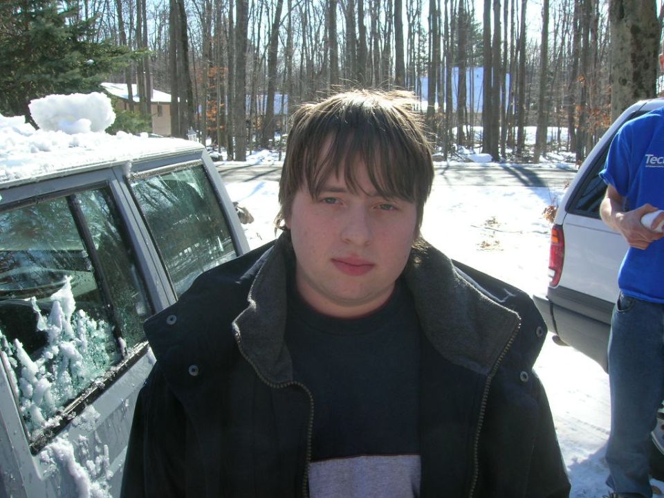 Person in foreground, snow-covered vehicle to the left, white vehicle to the right