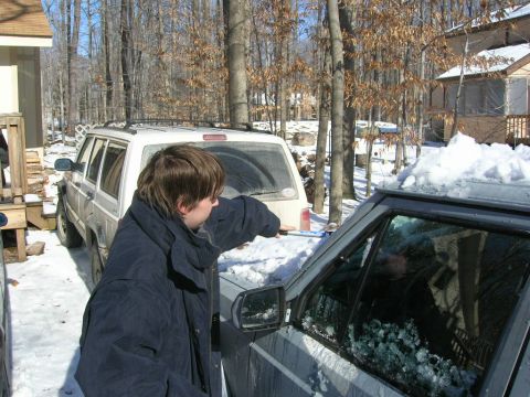 1993 Ford Probe - A person clears snow from the side window of a dark SUV, with a white SUV visible in the background during winter.