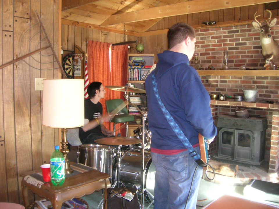 Two people in a room, one playing drums and the other holding a guitar