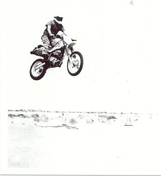 Motorcycle airborne during a jump, rider wearing helmet and camouflage pants