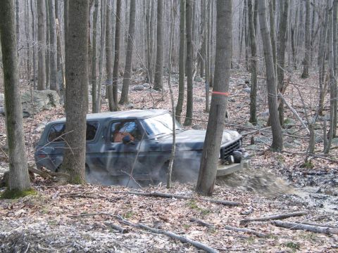 1995 Ford Bronco - This Ford Bronco is navigating a muddy trail through a dense forest.
