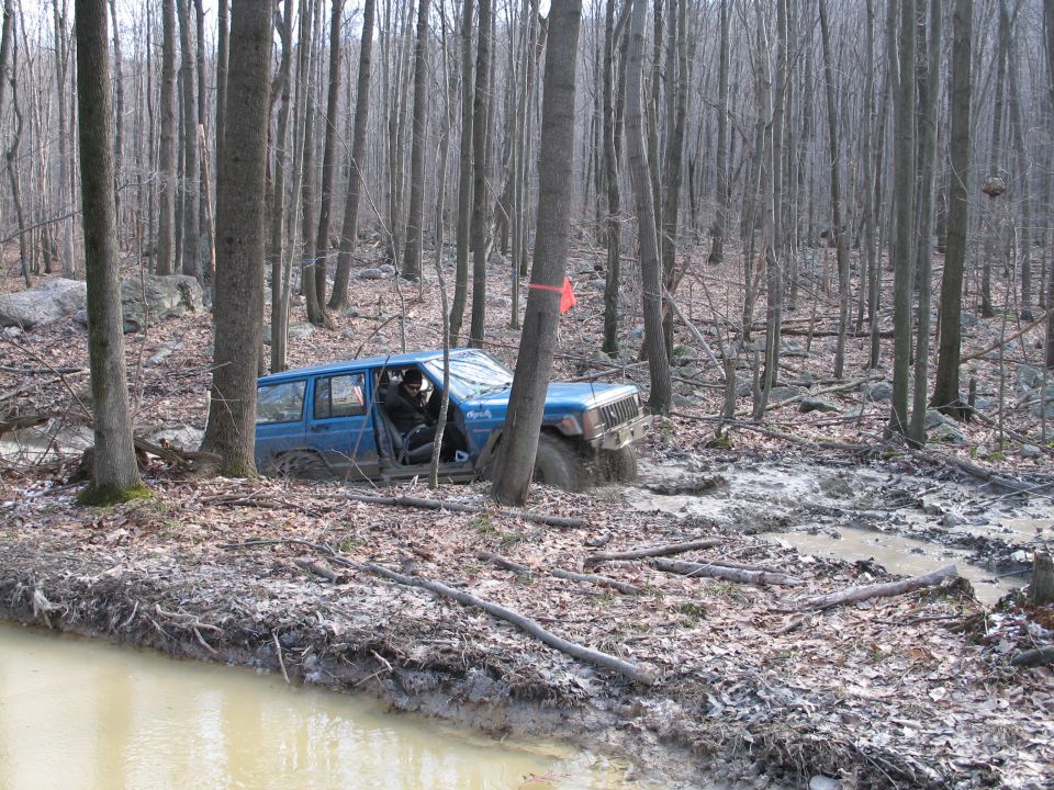 Blue Jeep Cherokee stuck in mud in a wooded area