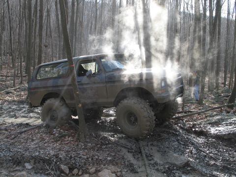 1995 Ford Bronco - This vehicle is navigating a challenging, muddy terrain in a dense forest environment.
