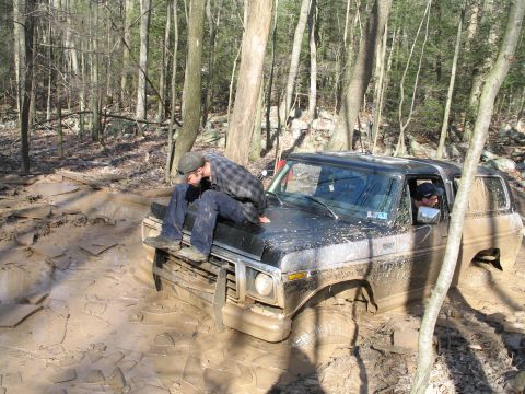 1995 Ford Bronco - Ford Bronco stuck in mud on a forest trail with a person on the hood.