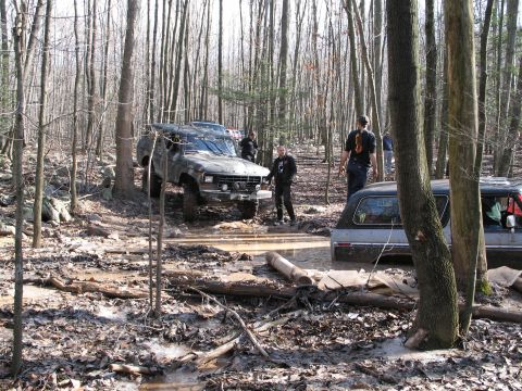 1995 Ford Bronco - Off-road vehicles navigate a challenging muddy trail in a wooded area.