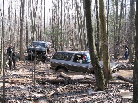 1995 Ford Bronco - Several off-road vehicles navigate a muddy forest trail.