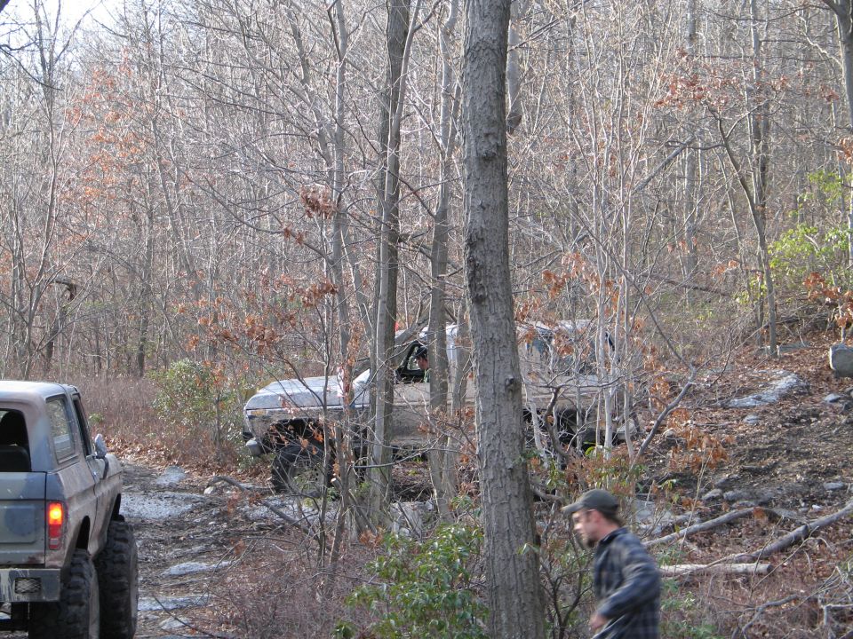 Dark blue Ford Bronco, lifted, off-road tires, rear view. Another SUV is visible behind it