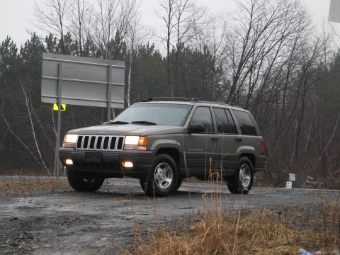 1995 Ford Bronco - A gray Jeep Grand Cherokee is seen from a three-quarter front view on a dirt road.