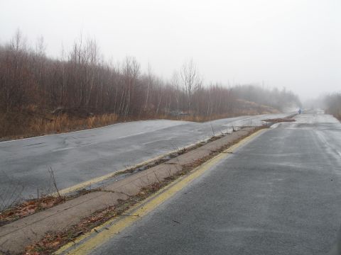 1995 Ford Bronco - A damaged road disappears into the fog, with trees lining the sides and a lone figure in the distance.