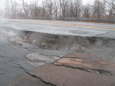 1995 Ford Bronco - A large pothole has formed on a road, with debris visible in the cavity and steam rising.