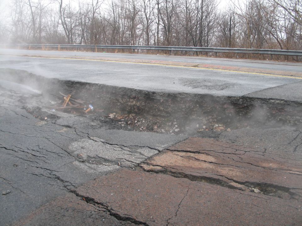 Road with a large pothole and debris, steam rising from the damaged asphalt
