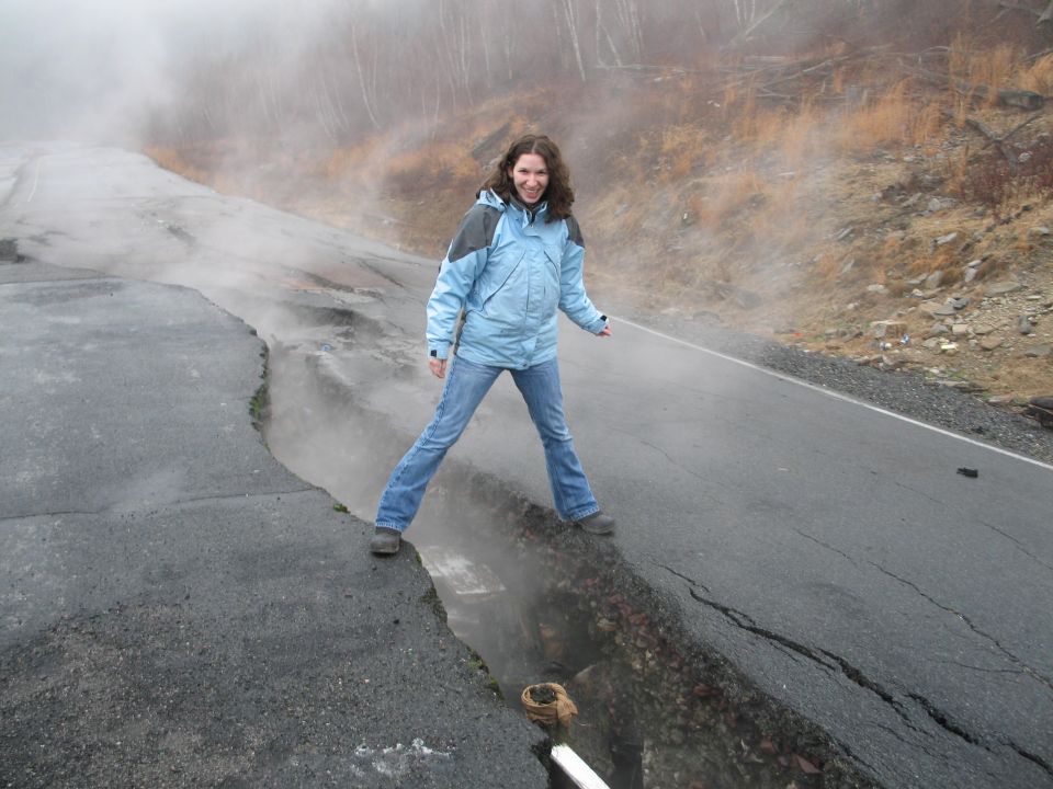 Woman stands on a damaged road with a large crack and steam rising