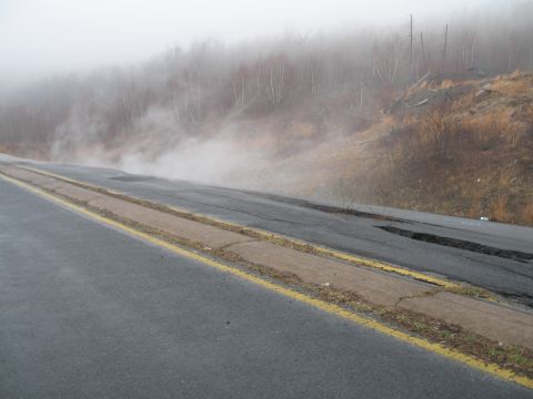 1995 Ford Bronco - A foggy scene shows steam rising from a damaged road shoulder, with trees visible in the background.