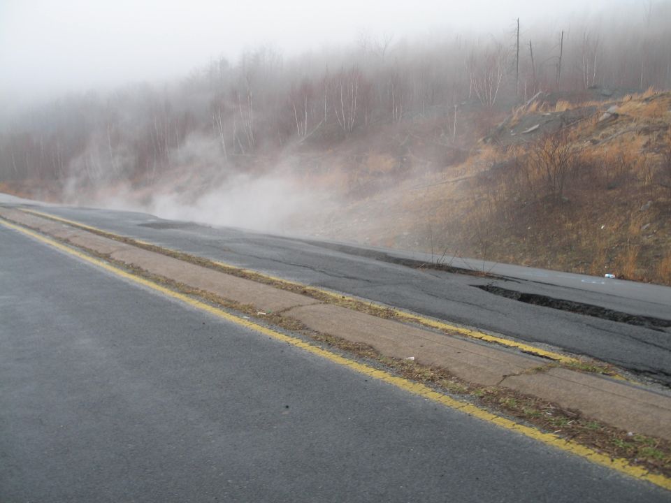 Foggy road with steam rising from the shoulder and cracked pavement