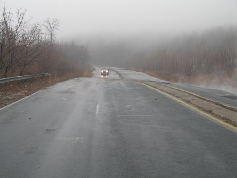 1995 Ford Bronco - A lone vehicle travels down a misty road, visibility low due to fog.