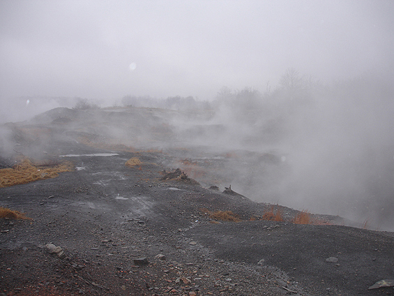 Misty landscape with grey gravel hills and patches of dry grass under an overcast sky