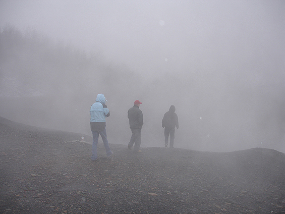 Three people walking on a gravel ridge in dense fog