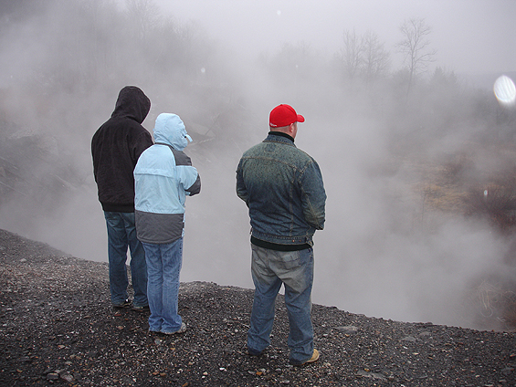 Three people from behind watching steam rise from a gravel bank