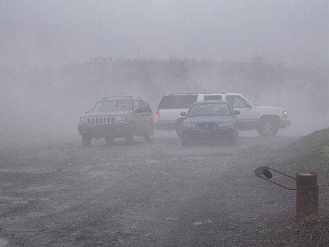 1979 Ford Bronco - Three vehicles parked in heavy fog on a gravel lot: a tan Jeep Grand Cherokee at left, a white full-size Chevrolet/GMC SUV with roof rack i…