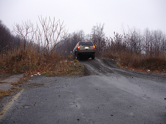 Rear of a dark gray SUV, brake lights on, climbing a gravel embankment