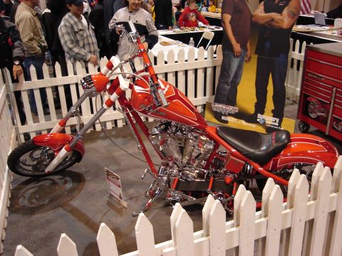 2000 Ford Crown Victoria - Custom chopper motorcycle on display at an auto show, surrounded by a white picket fence.
