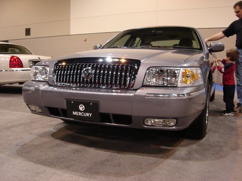 2000 Ford Crown Victoria - A silver Mercury Grand Marquis is displayed at an auto show with a child and adult nearby.