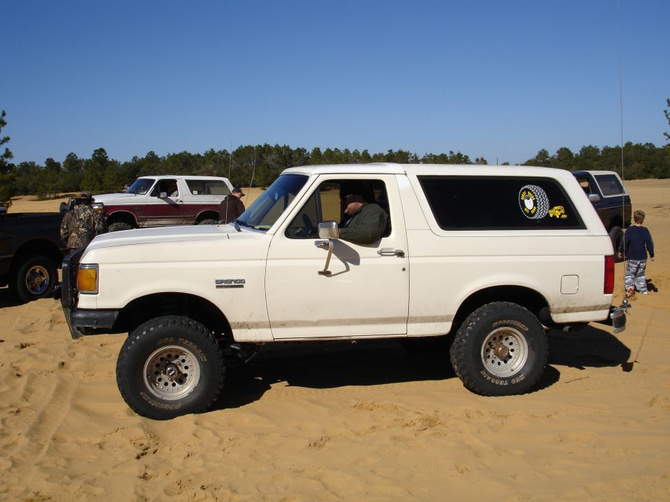 White 1989 Ford Bronco side view with off-road tires and a sticker on the rear window