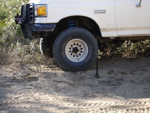 1989 Ford Bronco - A white 1989 Ford Bronco is shown with off-road tires and a brush guard, parked on sandy terrain.