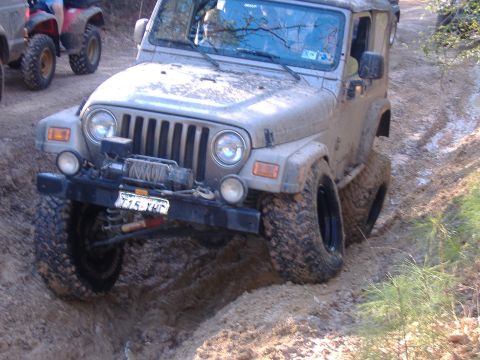 1999 Jeep Wrangler - A Jeep Wrangler navigates a muddy off-road trail, with another vehicle visible in the background.