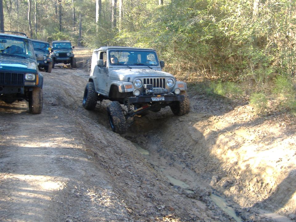 Silver 1999 Jeep Wrangler navigating a muddy off-road trail with other Jeeps